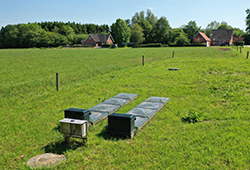 Grønt græsområde, der brydes af sorte firkanter der er bygget ned i jorden i 2 parallelle rektangler.
