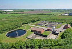 Dronefoto af nørre nebel renseanlæg. Der ses en rund tank i forgrunden, to bygninger og 3 aflange tanke i baggrunden