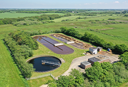 Dronefoto af Outrup renseanlæg. Der ses en rund tank og to aflange tanke.