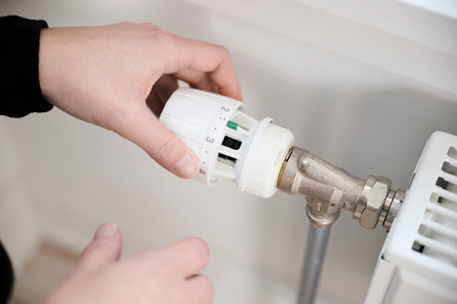 Foto af hånd, der drejer fjernvarmetermostat på radiator